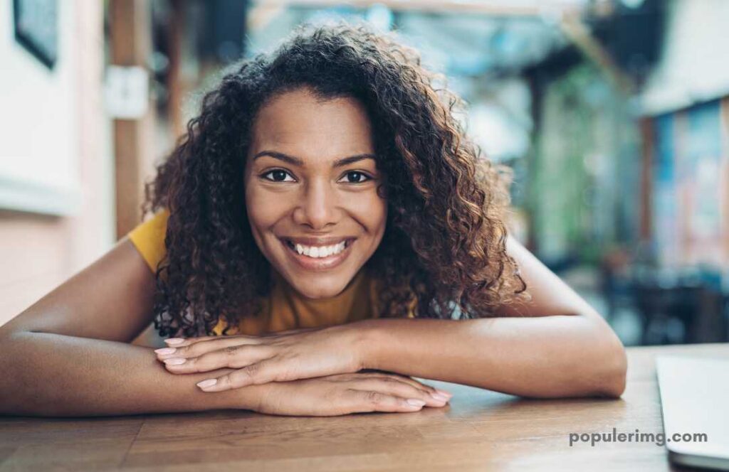 Smiling Girl Showing Teeth With Hands-On Table 