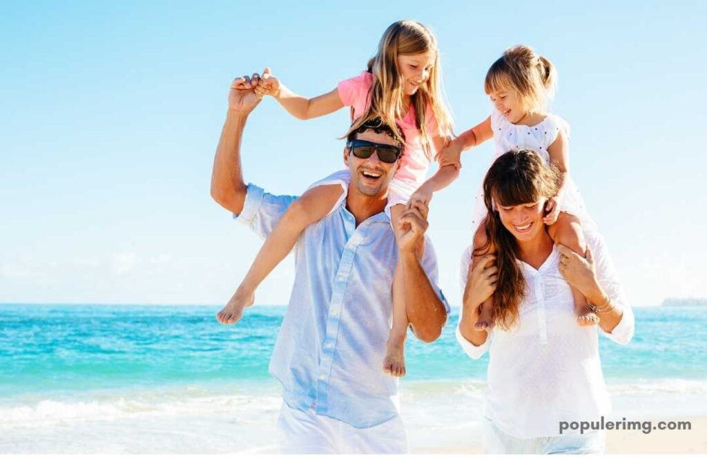 Father Carrying His Older Daughter On His Shoulders And Mother Carrying Her Younger Daughter On His Shoulders