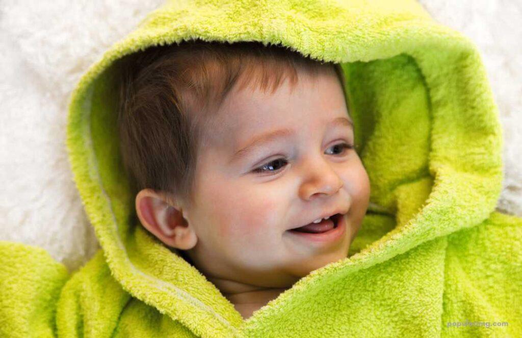 A Baby In A Green Hooded Towel Laying On A White Blanket.	