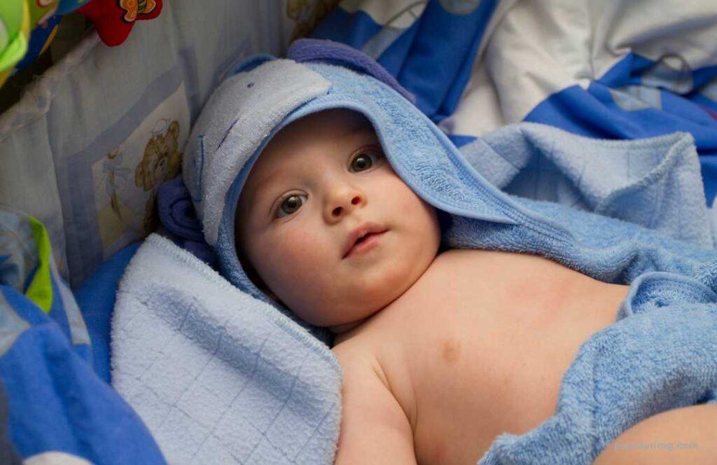 A Baby Laying In A Blue Towel.	