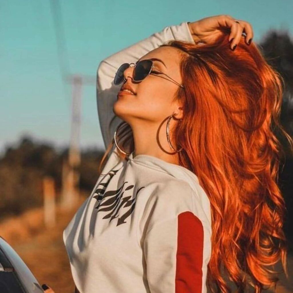 a woman with red hair leaning against a car.	